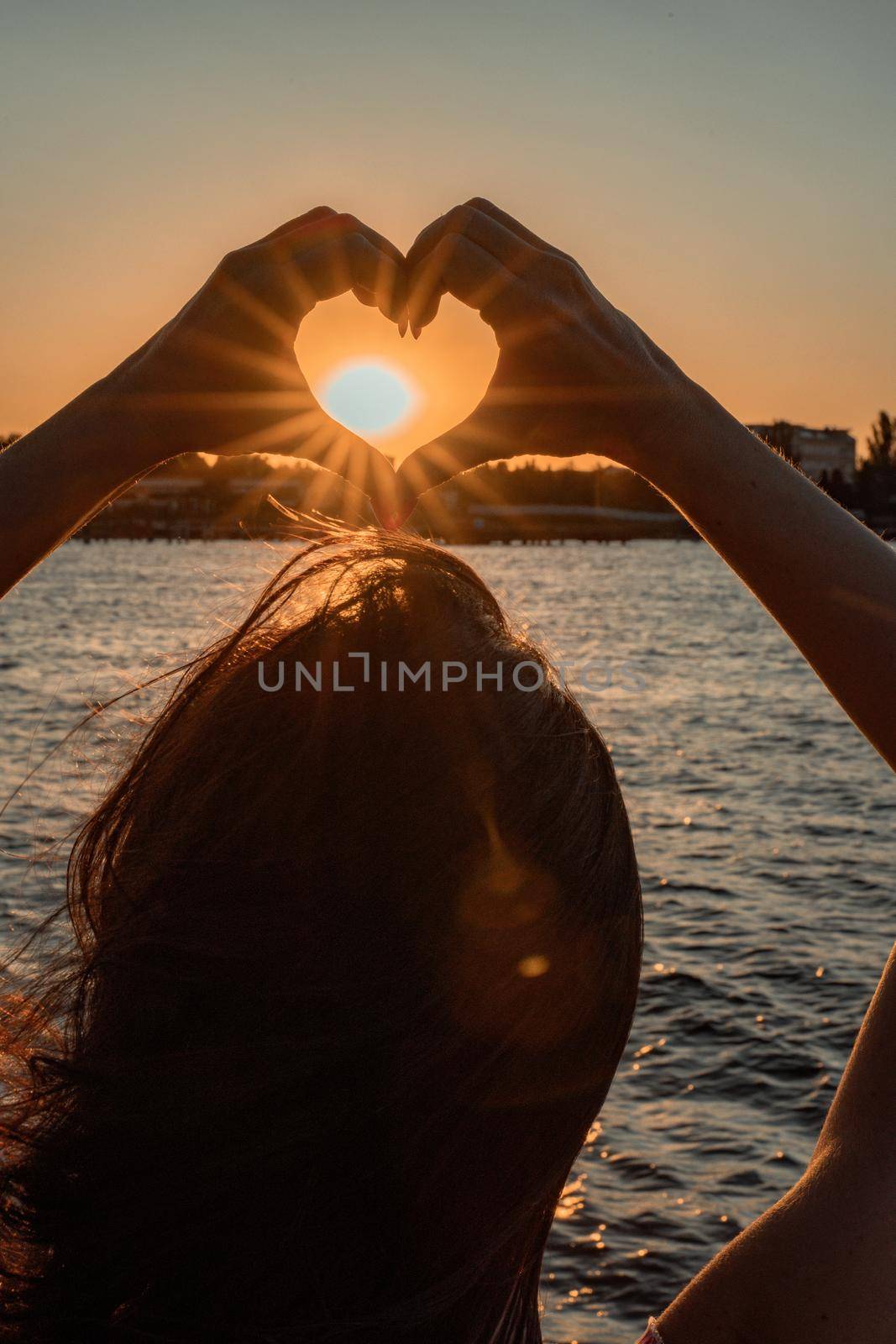 Silhouette against the sunset - hands folded in the shape of a heart. Sun with rays between the palms. Concept for Valentine's Day, declaration of love. Minimalism, space for text, warm colors