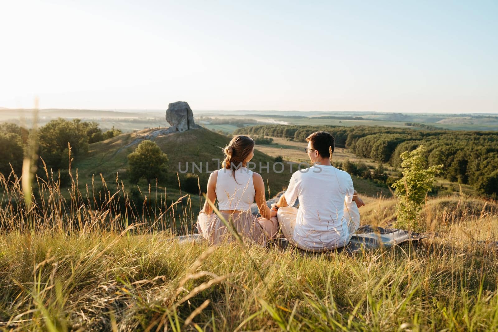 Man and Woman Practicing Yoga and Meditation Outdoors at Sunset with Scenic Landscape and Nature Miracle Giant Stone on the Background by Romvy