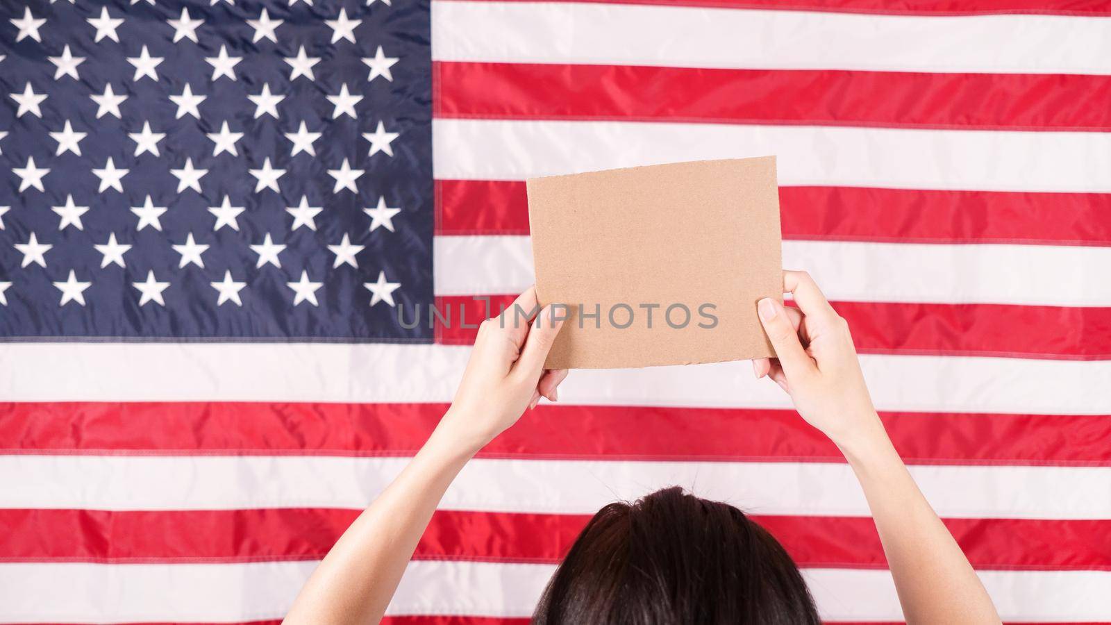 Woman is holding an empty cardboard with Space for Text sign US flag on background. Protest against anti abortion law. Women's strike. Womens rights freedom. Against racism racial discrimination.