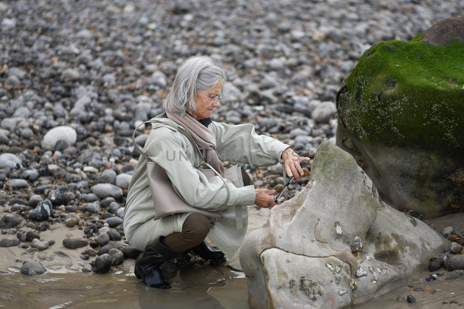 Gray-haired woman makes photo on smartphone at the ocean