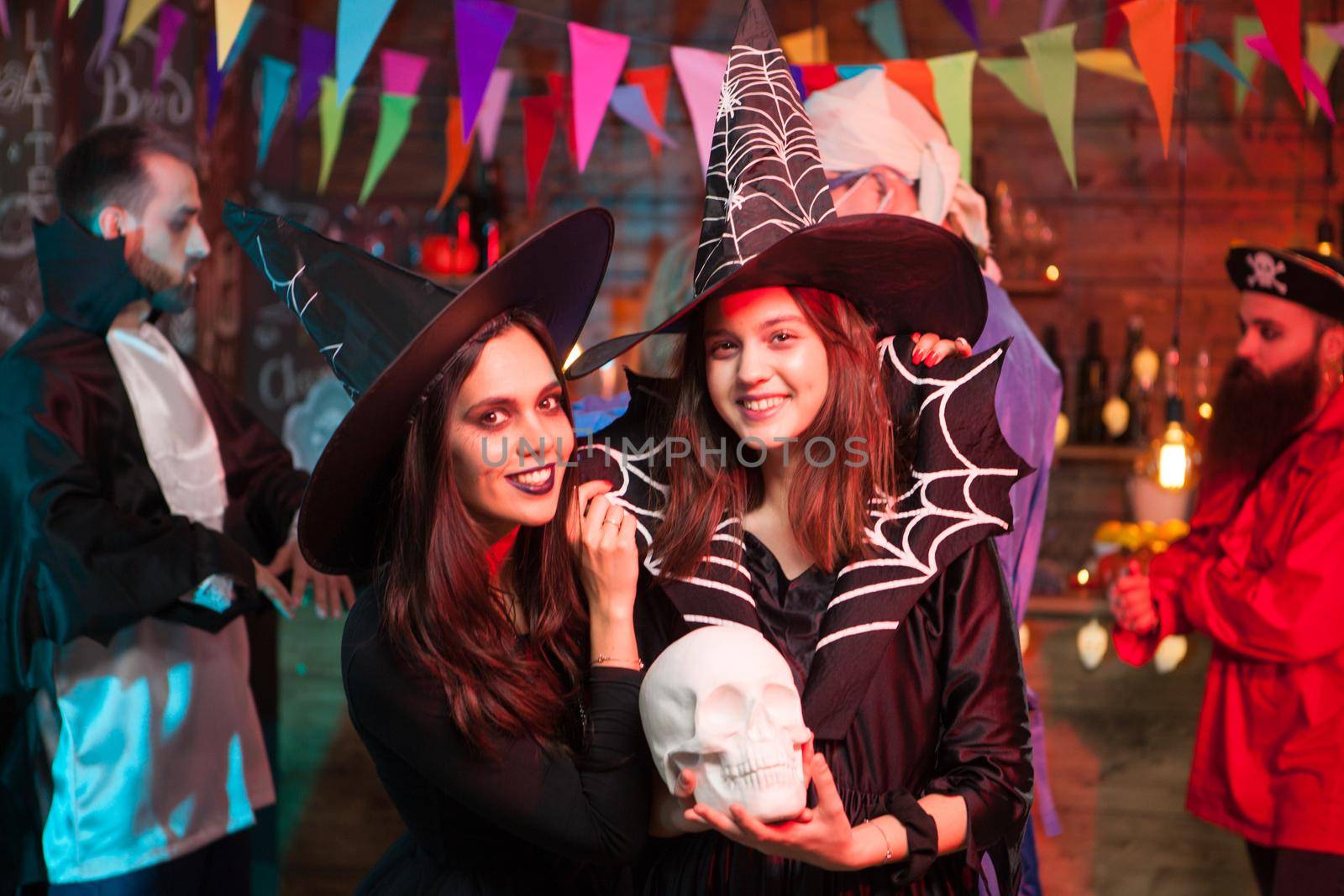 Beautiful young witch holding a human skull and smiling to the camera at halloween party by DCStudio