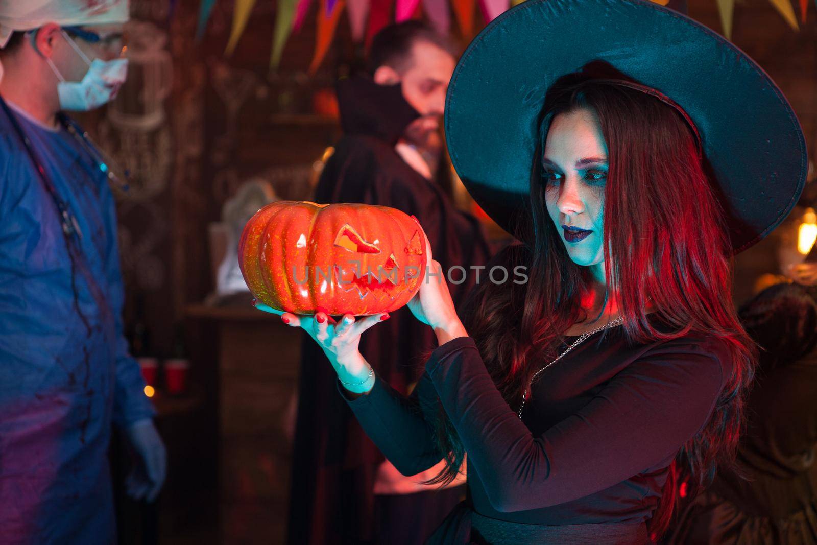 Portrait of beautiful woman dressed up like a witch doing dark magic on a pumpkin for halloween by DCStudio