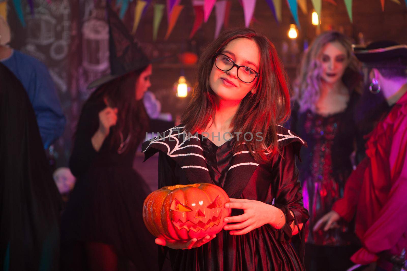 Young and creepy girl dressed up like a witch holding a pumpkin at halloween celebration by DCStudio