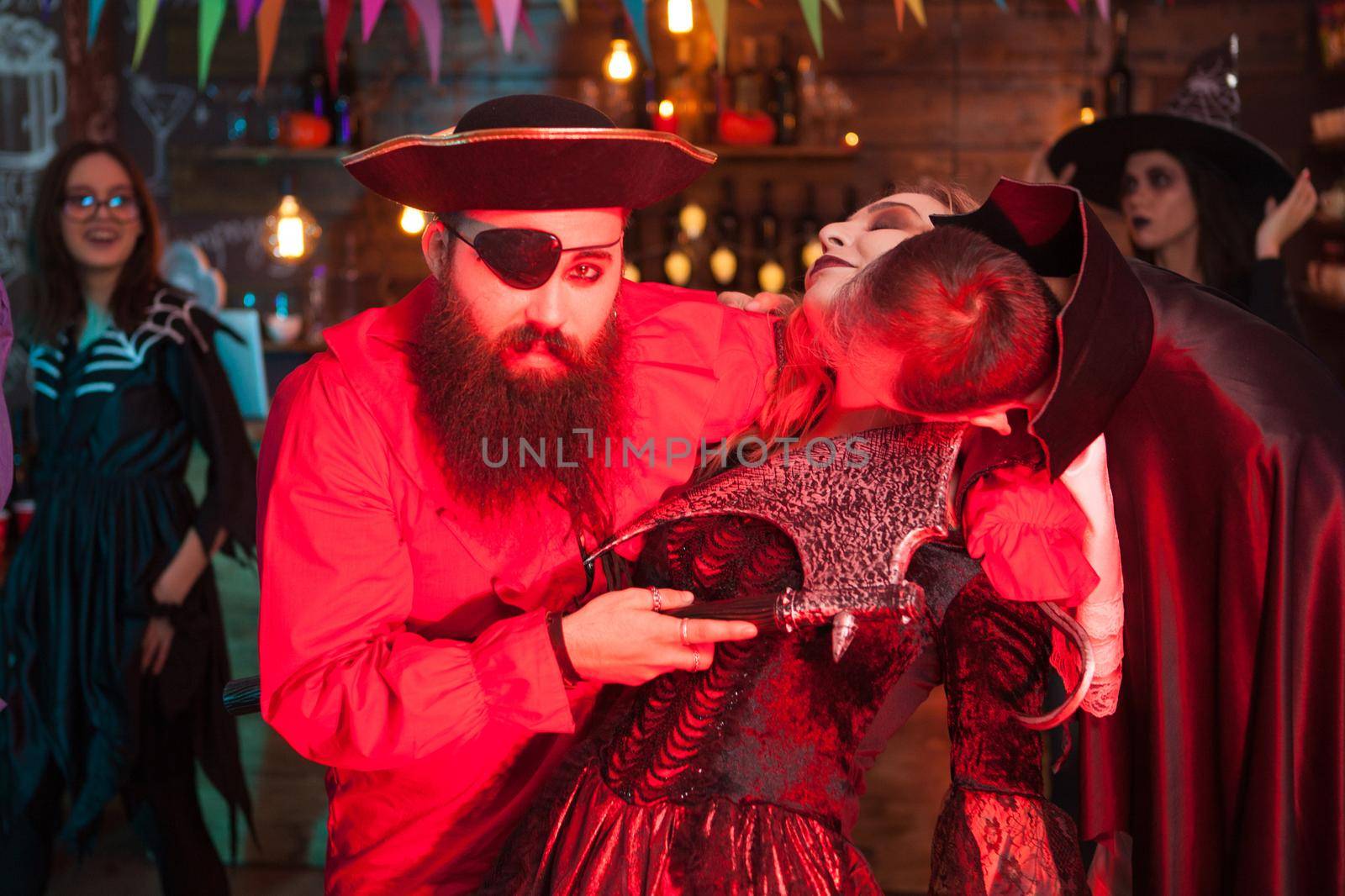 Man in dracula costume biting woman's neck dressed up like a witch for halloween. Man in pirate costume.
