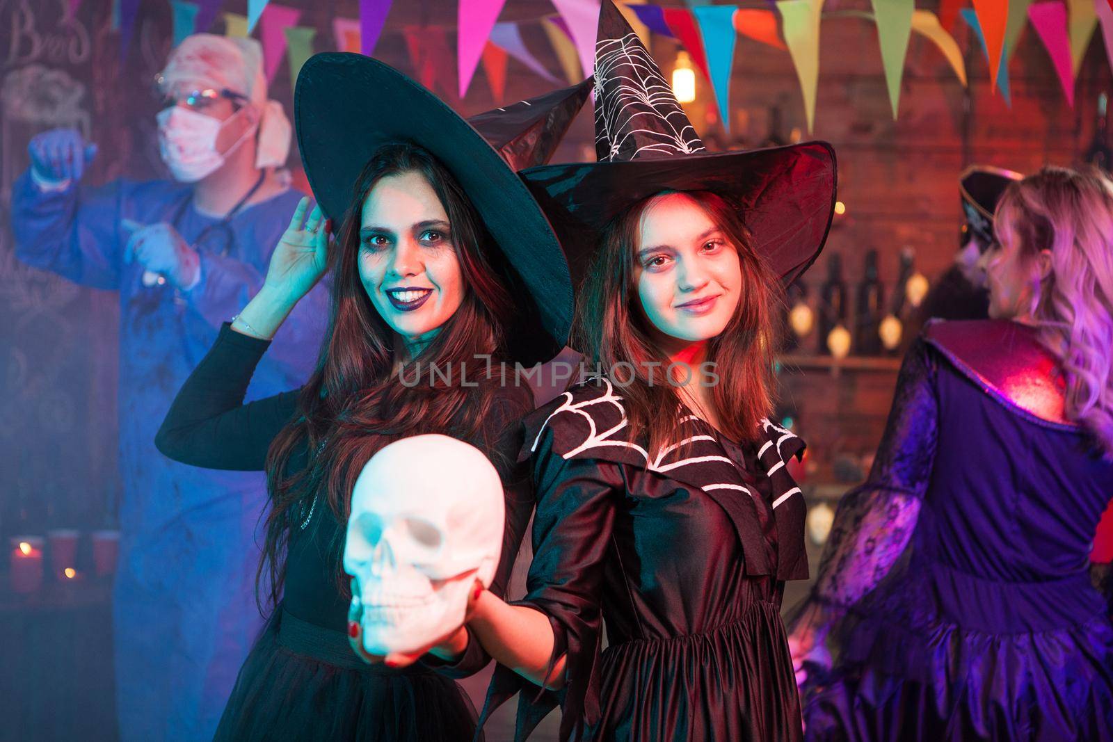 Sisters dressed up like witches at a halloween party holding a skull. Witches gathering. Halloween costume.