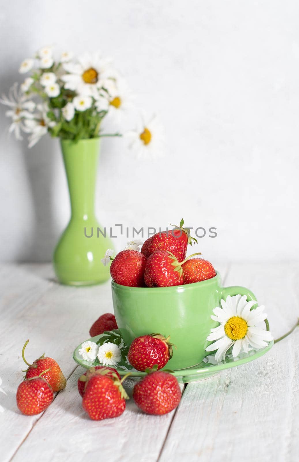 ripe strawberries from the garden in a green mug with white chamomile, fruity summer still life, close-up. High quality photo