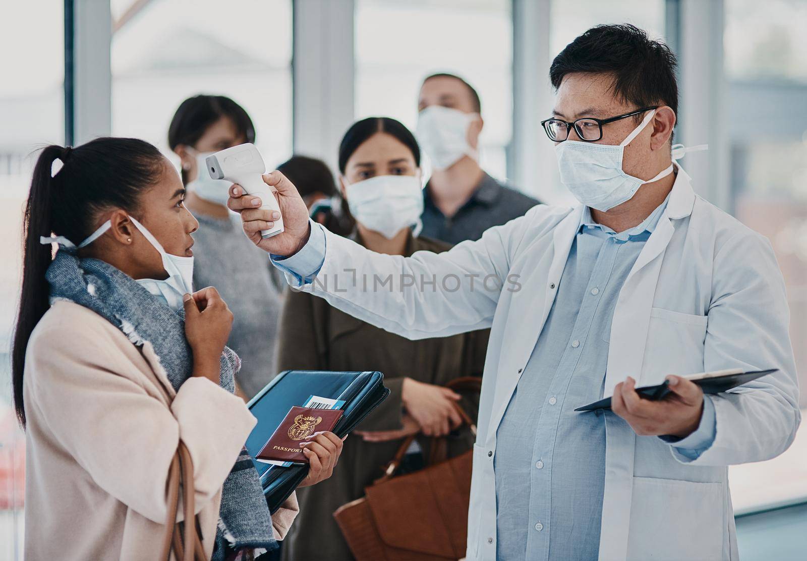 A travel healthcare worker testing covid temperature at the airport using an infrared thermometer. Medical professional doing a coronavirus check on a woman at an entrance to prevent the spread.