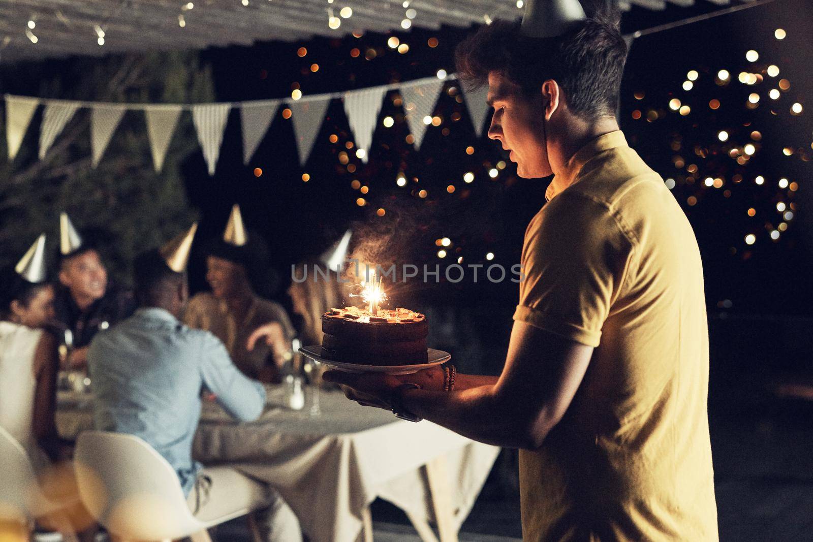 Trying my best to not drop the birthday cake. a handsome young man carrying a cake at a birthday celebration with friends outdoors in the evening. by YuriArcurs