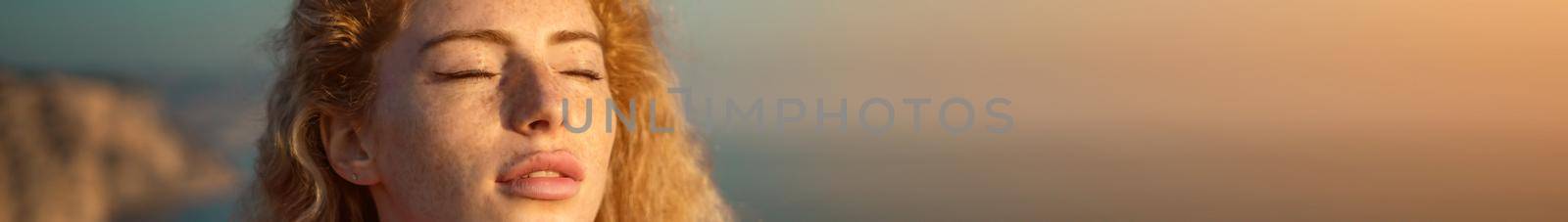 Women's eyes banner. Close up portrait of curly redhead young caucasian woman with freckles at sunset time and sea background. Cute woman portrait. by panophotograph