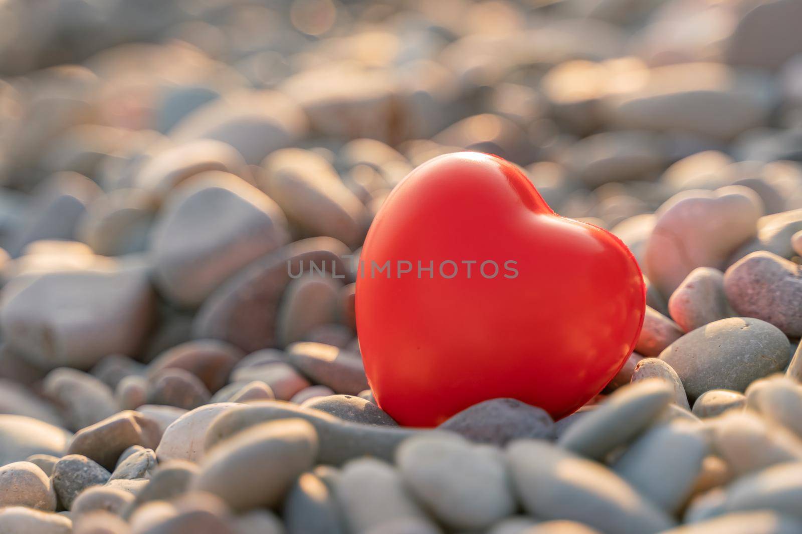 Valentine's Day concept. Red heart romantic love symbol on pebble beach at sunset with copy space. Template for inspirational compositions and postcards with quotes