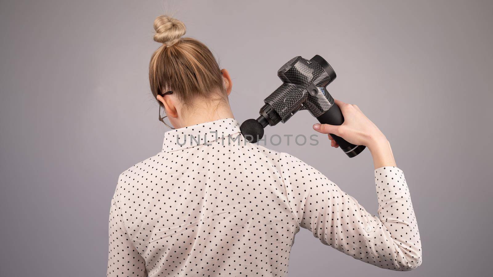 Caucasian business lady makes herself a back massage with a massager gun on a white background