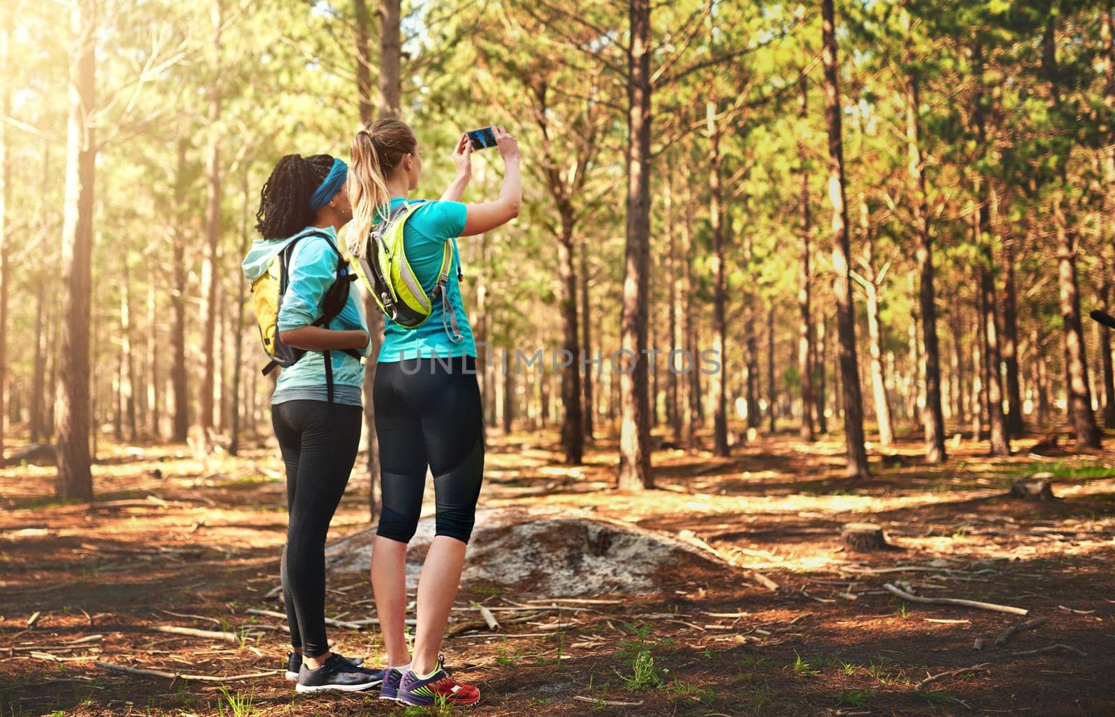 Take nothing but memories with you. two sporty young woman taking pictures while out in nature. by YuriArcurs