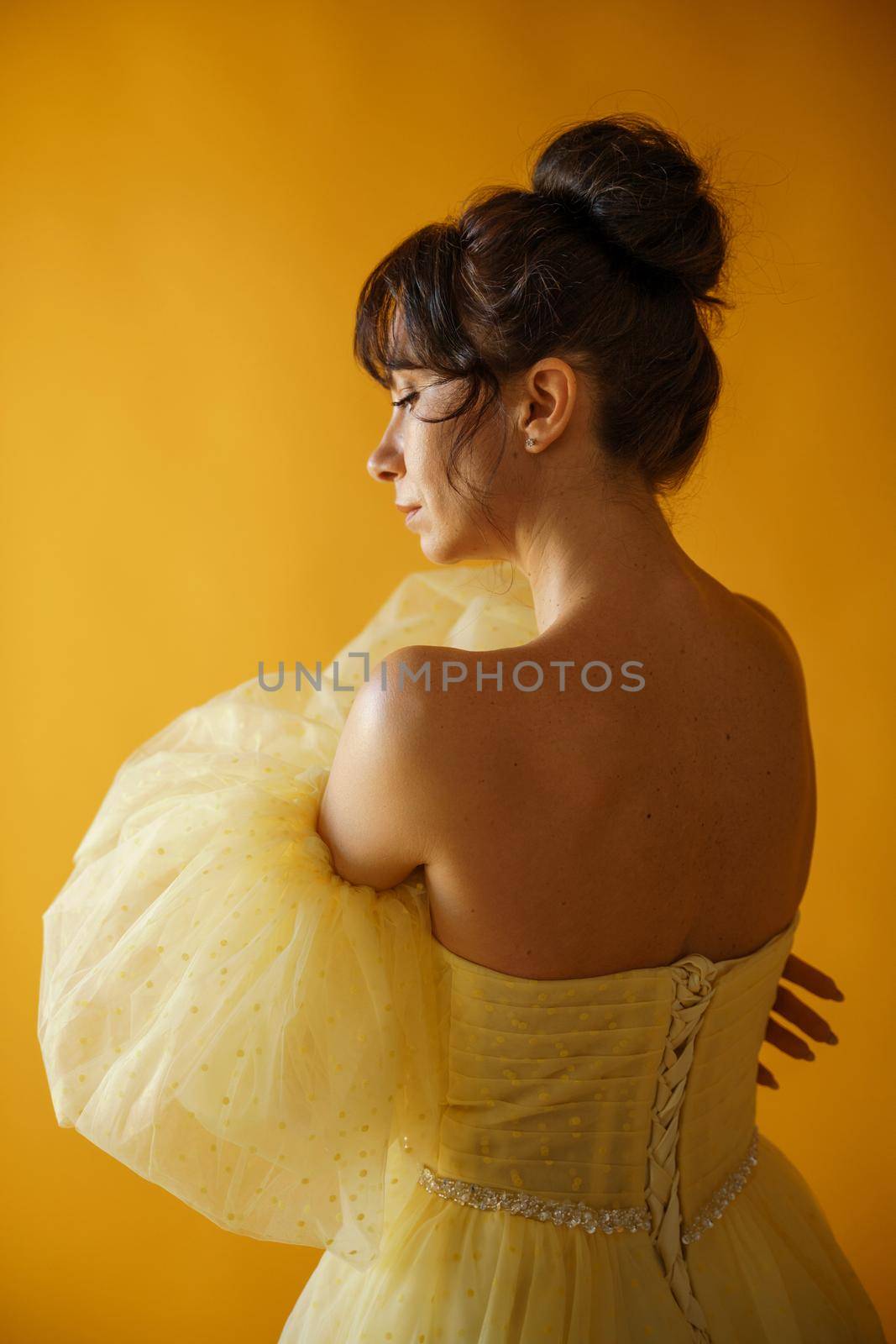 Profile portrait of a beautiful middle-aged woman in a yellow dress, her hair pulled up against a yellow background.