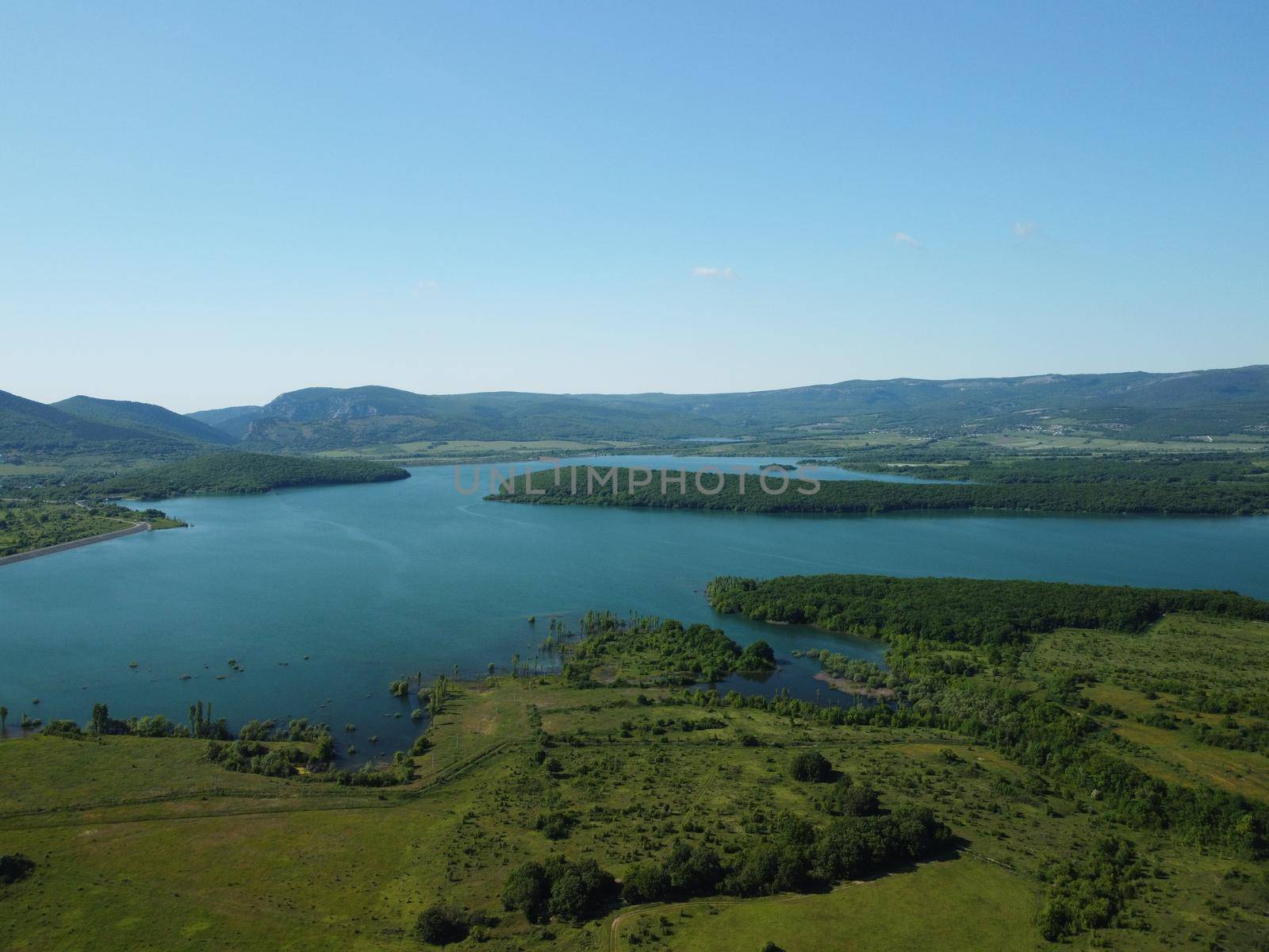 Aerial landscape from flying drone storage reservoir at mountain foot covered colorful spring forest. Beautiful view from above blue lake among highlands