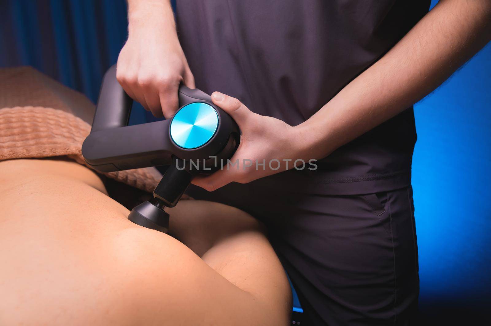 Physiotherapist treats the spine and back of a man with a massage percussion device. Physiotherapy, close-up, massage therapist.
