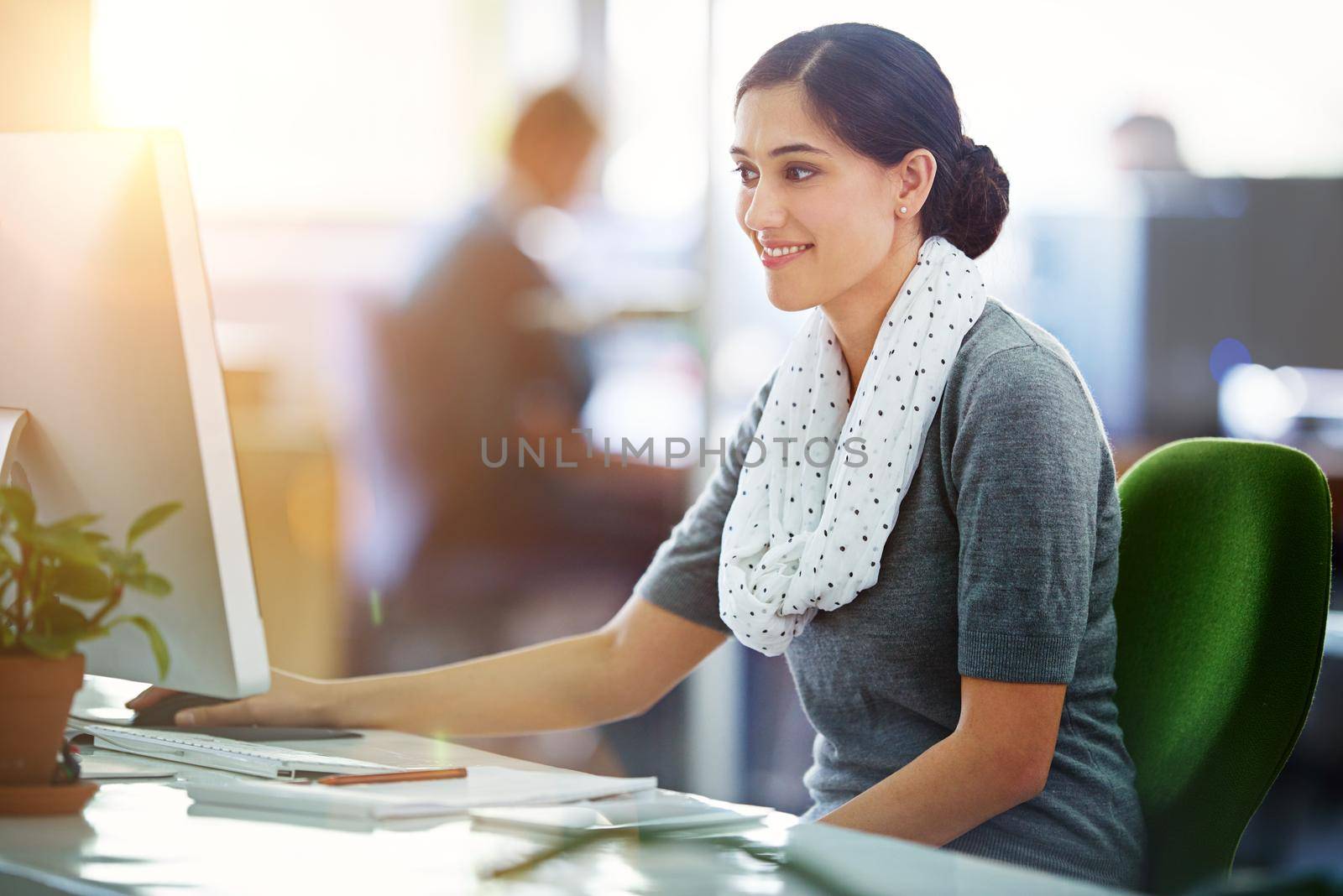 Young smiling female designer working on a computer in a modern office. Creative woman at her work desk browsing inspiration for designs on a pc at the workplace, over copy space background