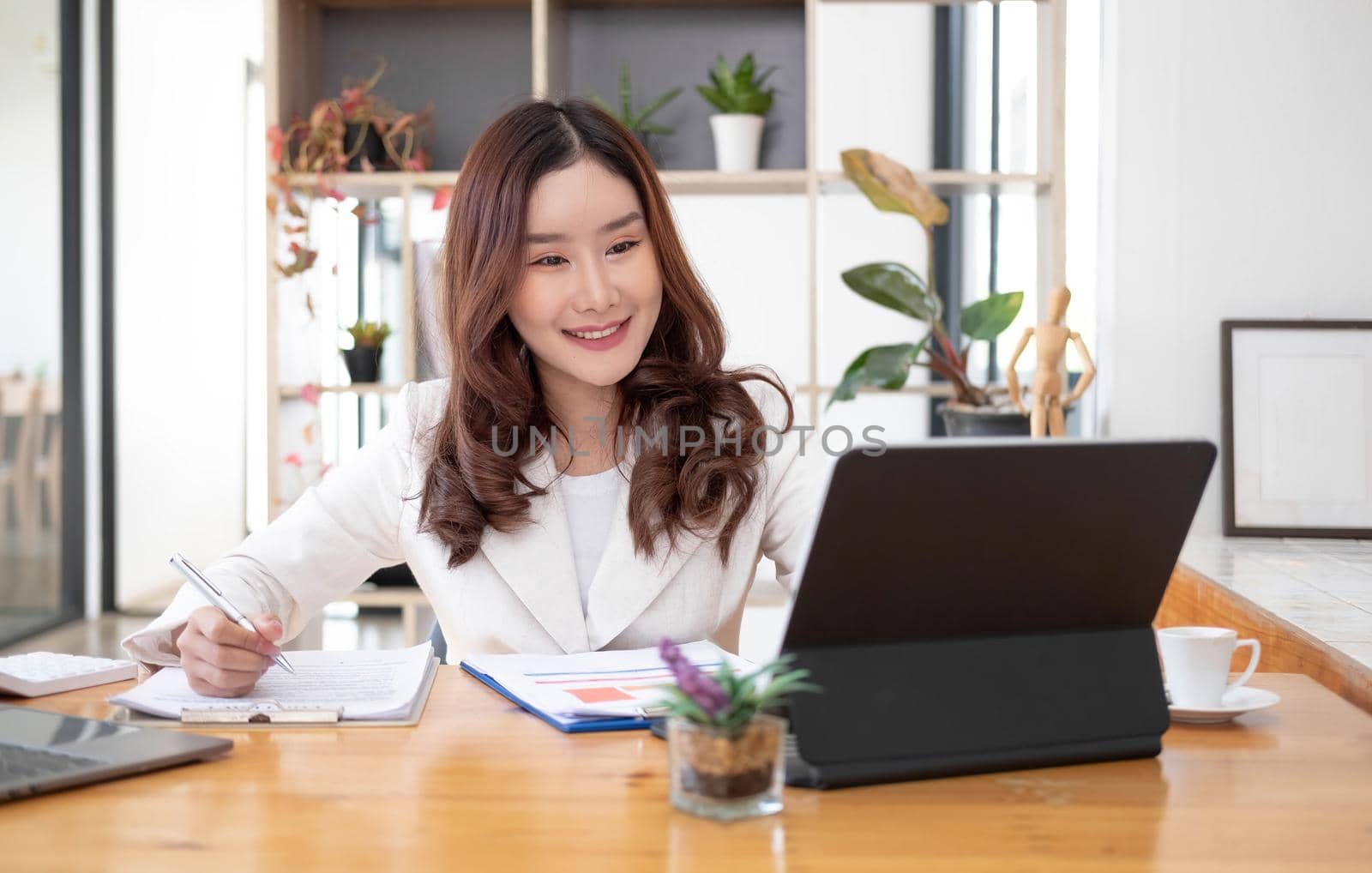 Beautiful Asian businesswoman analyzes charts using laptop calculator at the office..