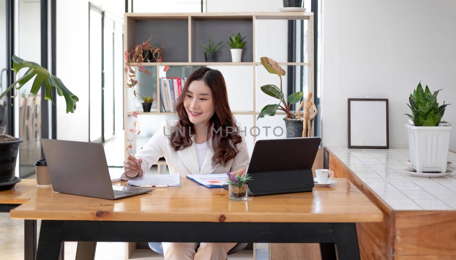 Beautiful young asian woman sitting at coffee shop using laptop. Happy young businesswoman sitting at table in cafe with tab top computer. by wichayada