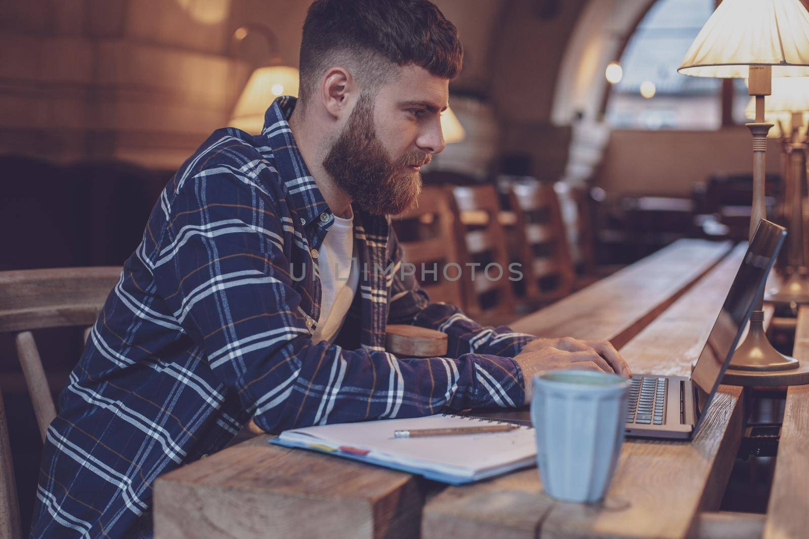 Young professional surfing the Internet on his laptop with cup of coffee on table at coffee shop or home office, working from cafe concept