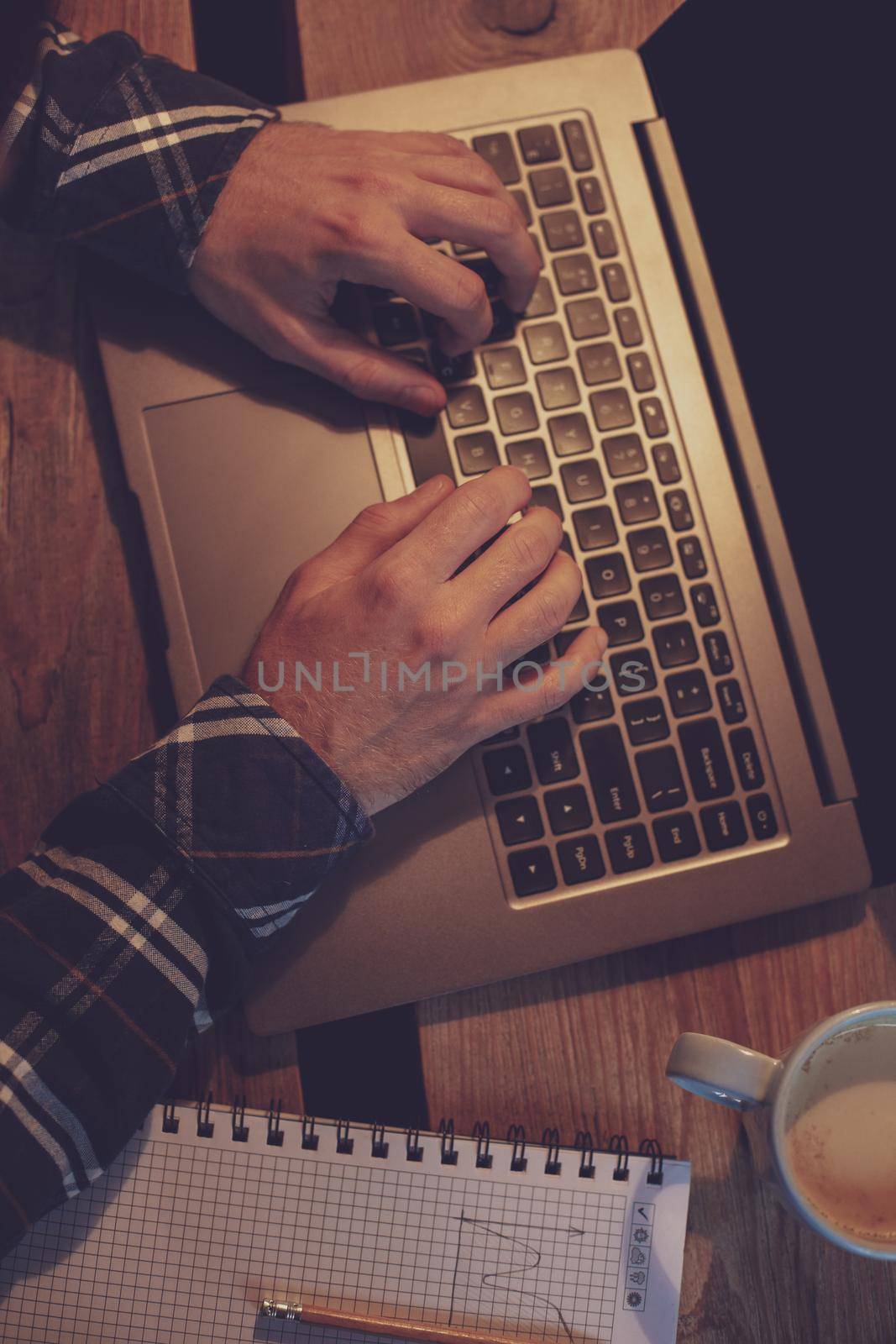Young man drinking coffee in cafe and using laptop. Man's hands using laptop during coffee break. Working from cafe concept