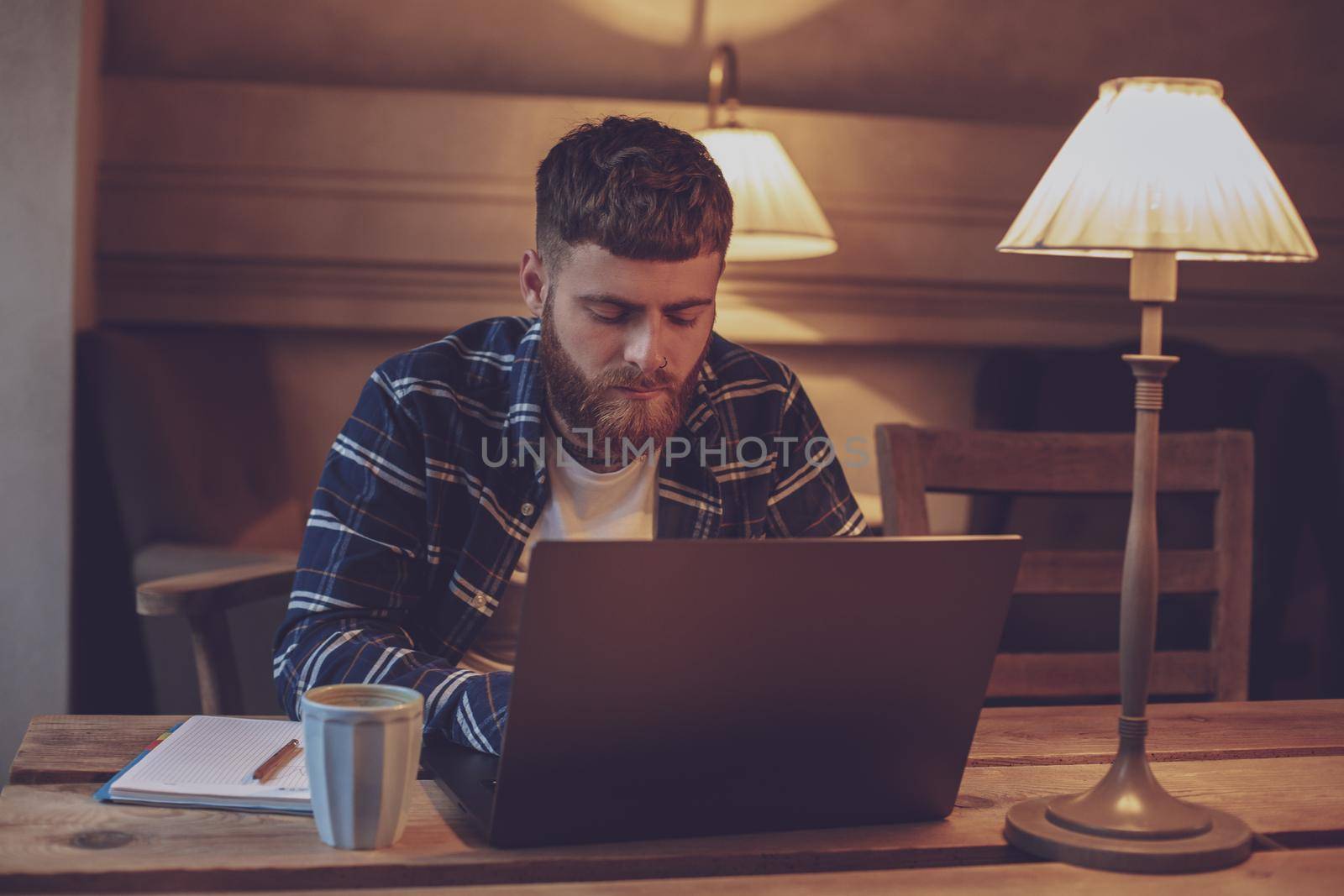 Young professional surfing the Internet on his laptop with cup of coffee on table at coffee shop or home office, working from cafe concept