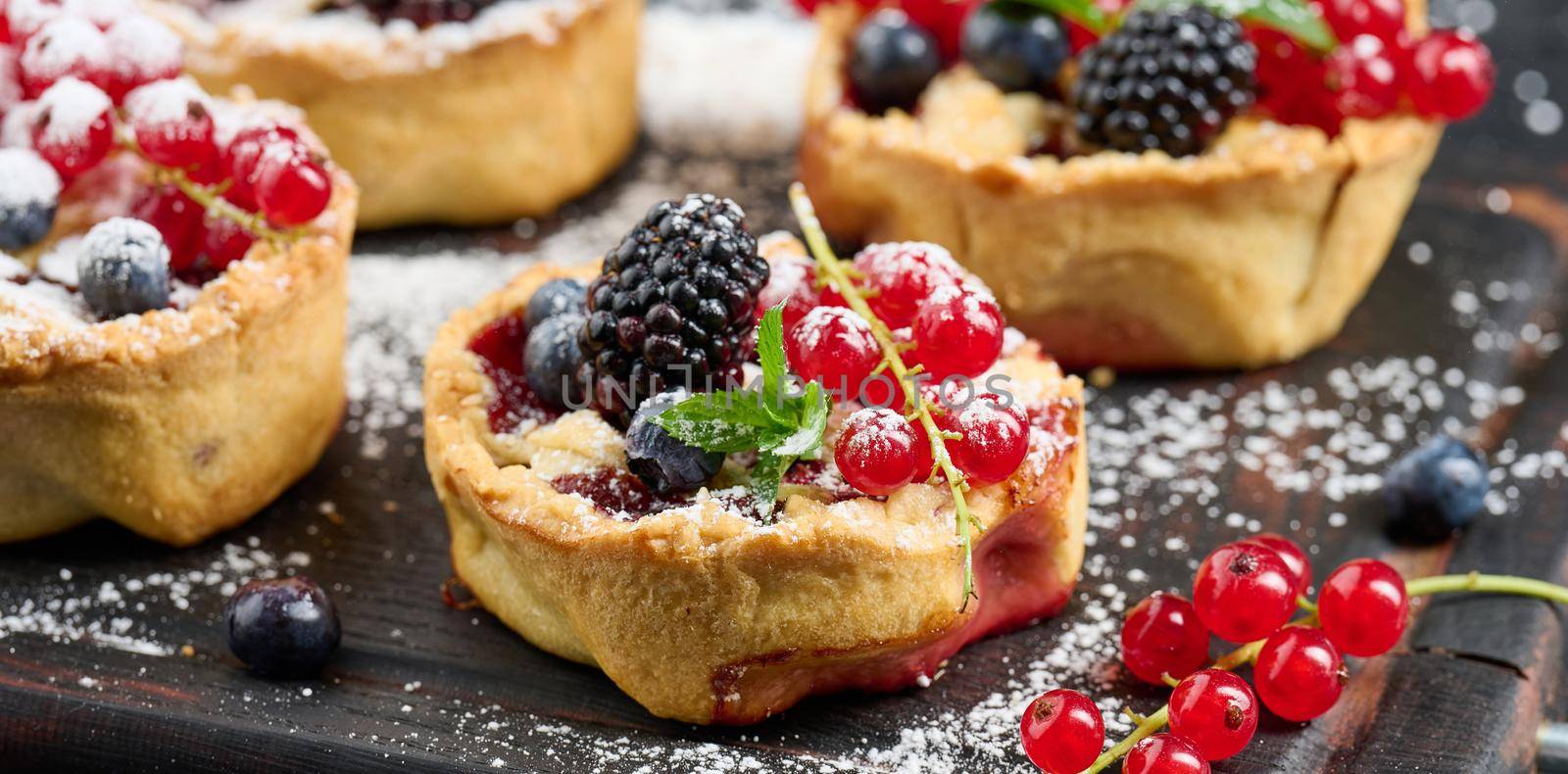 Fruit tart with red currants sprinkled with powdered sugar on a black table