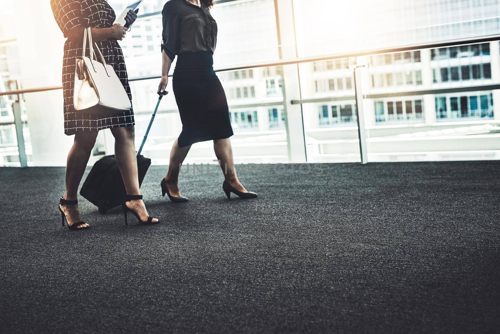 Shes come all the way to meet with success. two unrecognizable businesswomen walking together with their bags in a modern workplace. by YuriArcurs