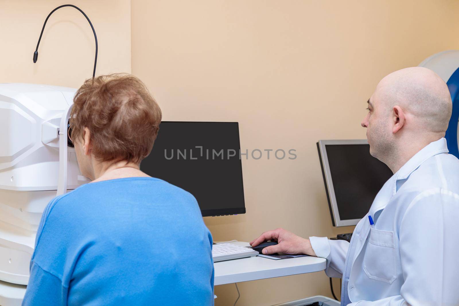 A male ophthalmologist checks the eyesight of an adult woman using a modern device.