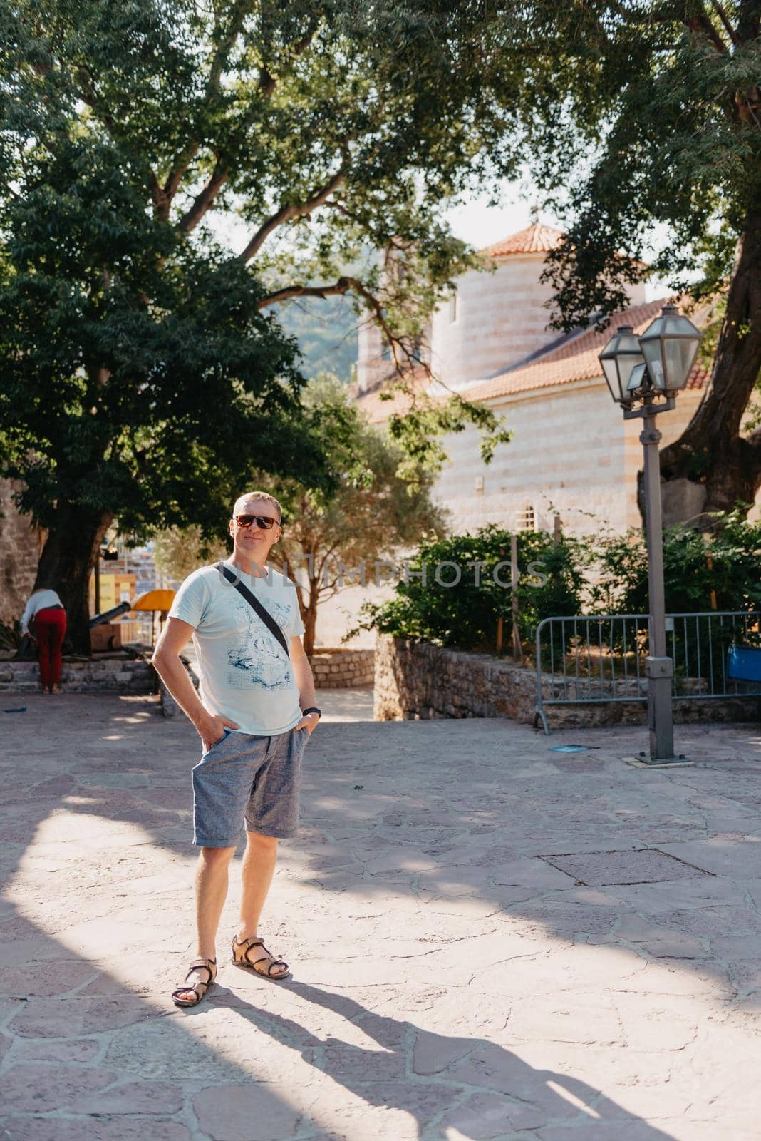 A handsome young man standing and smiling happily in the background of urban buildings. Forty years old caucasian tourist man outdoor near old city buildings - summer holiday. by Andrii_Ko