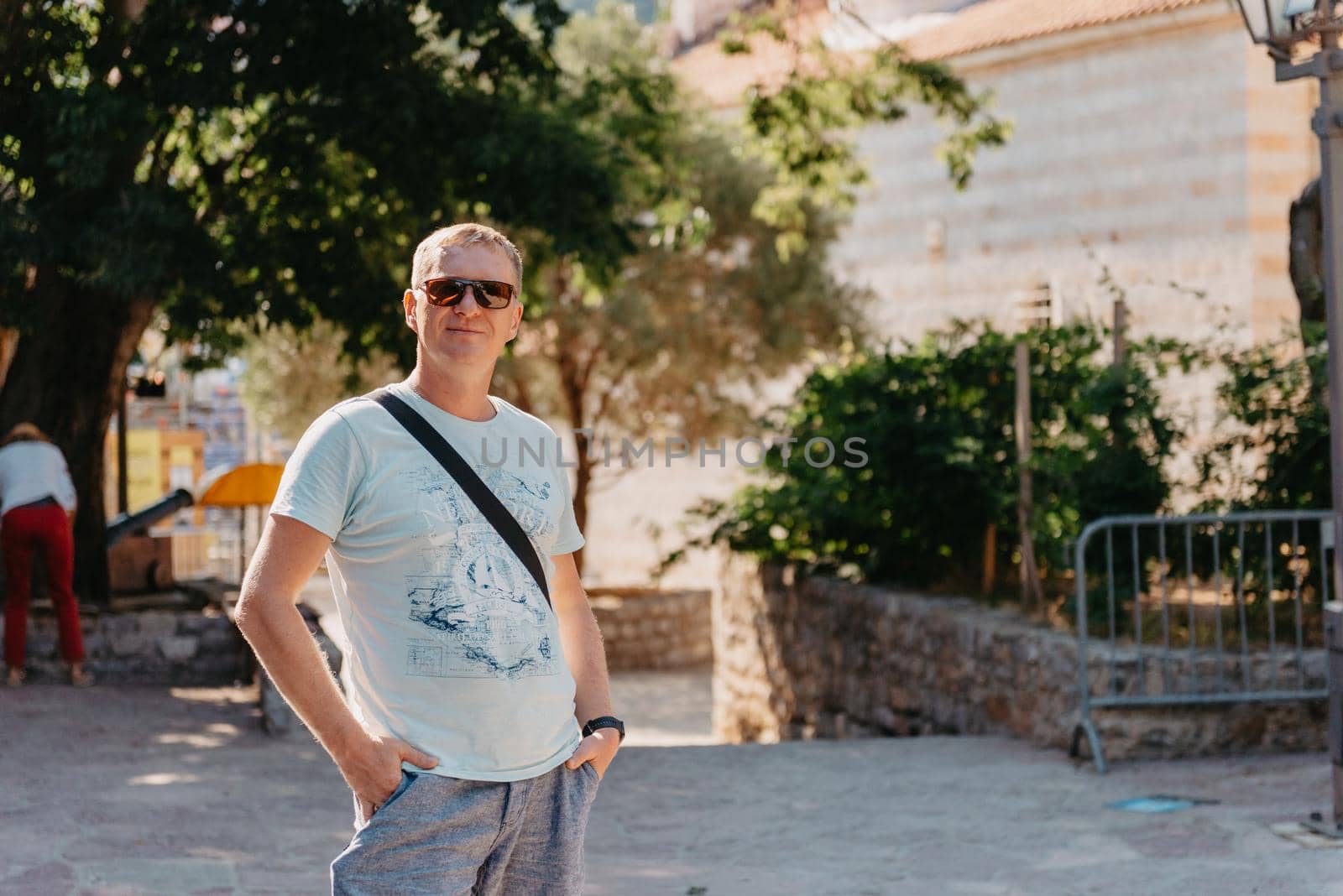 A handsome young man standing and smiling happily in the background of urban buildings. Forty years old caucasian tourist man outdoor near old city buildings - summer holiday.