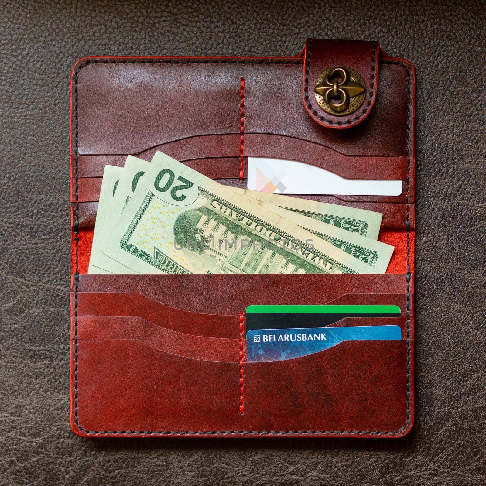 Open red leather clutch with money and credit cards on brown leather background.
