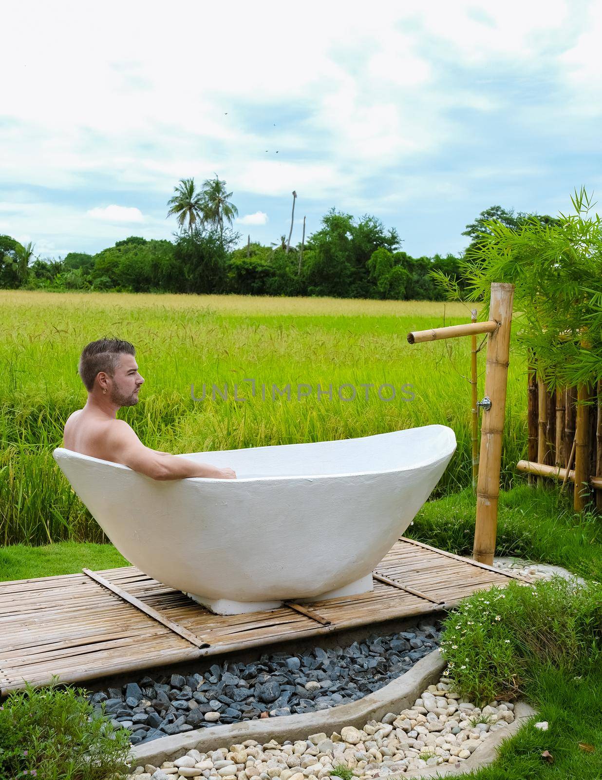 men in a white bathtub outside looking out over a green rice field, men and women in bath tub outside on vacation at a homestay in Thailand with green rice paddy field