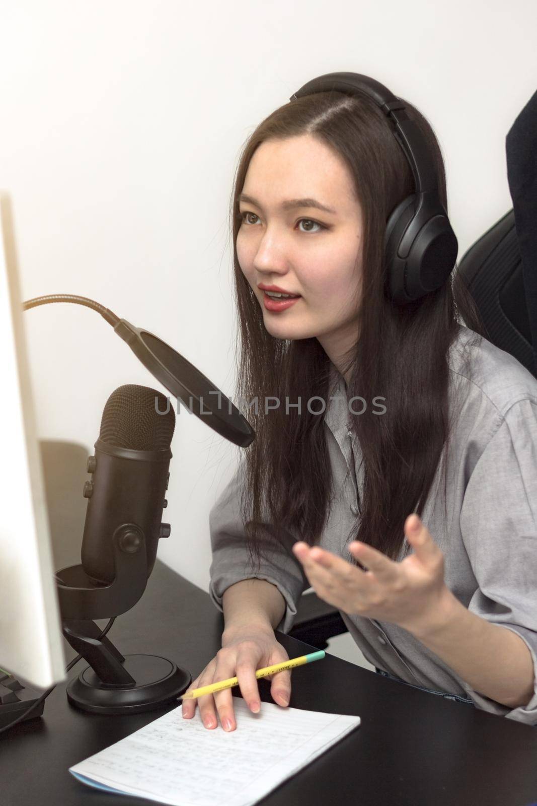 Young millennial woman with professional microphone and headphones recording podcast at studio, technology and media concept, vertical image, selective focus