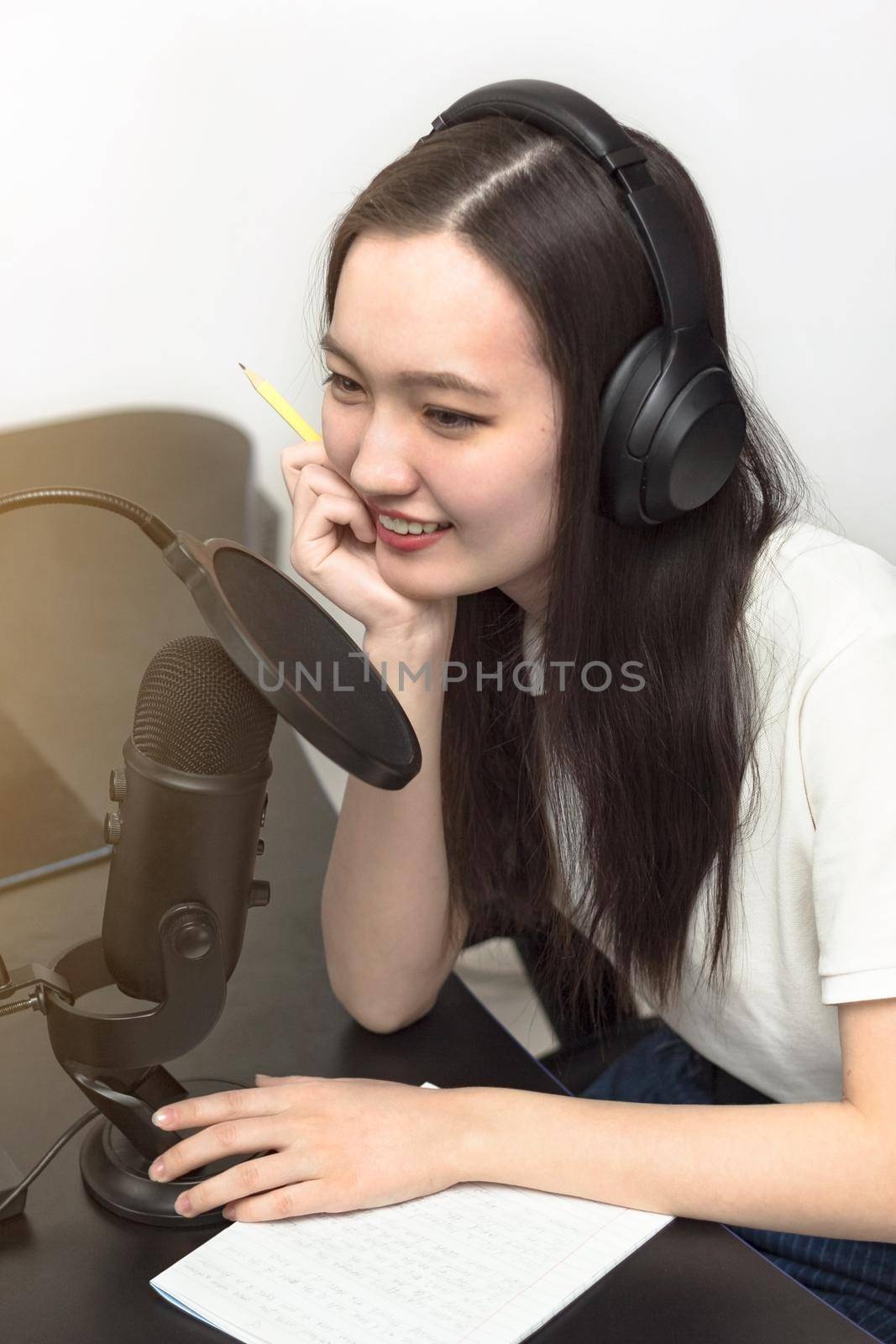 Young smiling millennial woman with professional microphone and headphones recording podcast at studio, technology and media concept, vertikal image