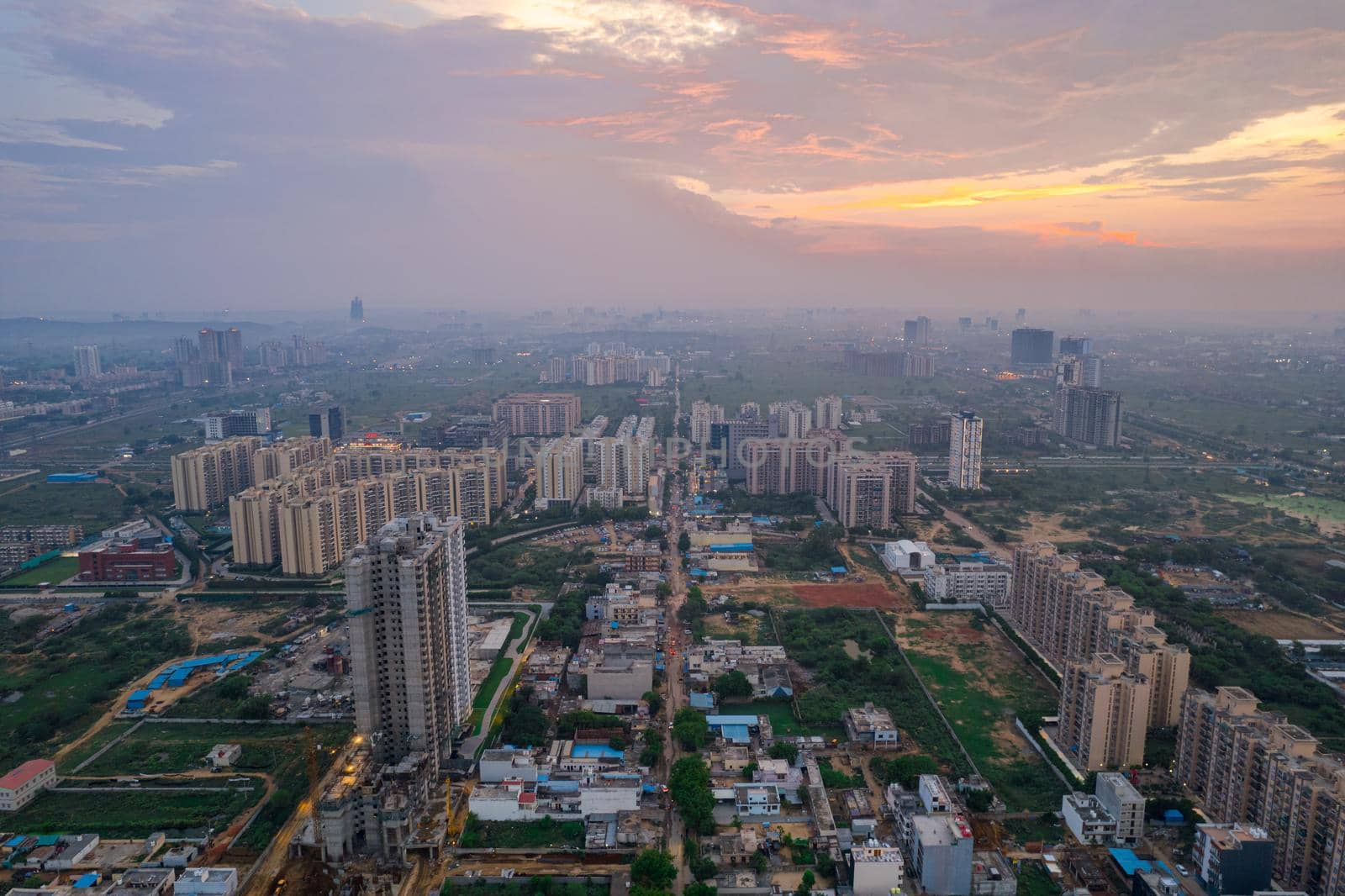 drone aerial shot showing busy traffic filled streets between skyscrapers filled with houses, homes and offices with a red sunset sky showing the hustle and bustle of life in Gurgaon, delhi by Shalinimathur