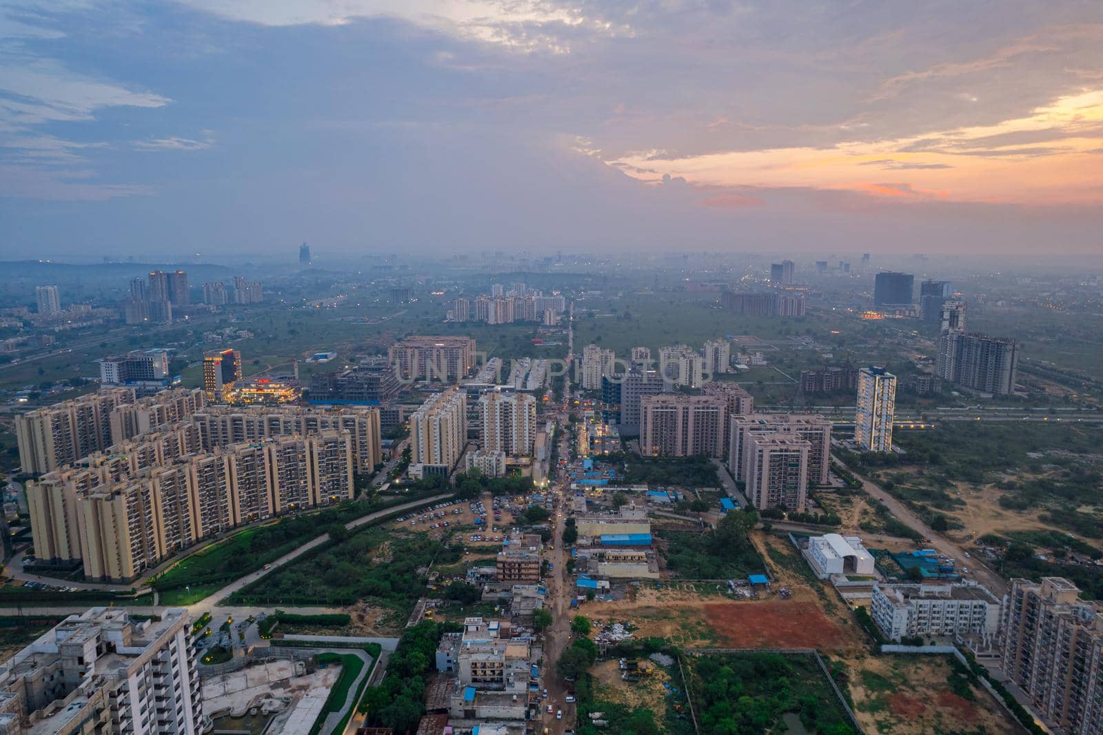 drone aerial shot showing busy traffic filled streets between skyscrapers filled with houses, homes and offices with a red sunset sky showing the hustle and bustle of life in Gurgaon, delhi drone shot