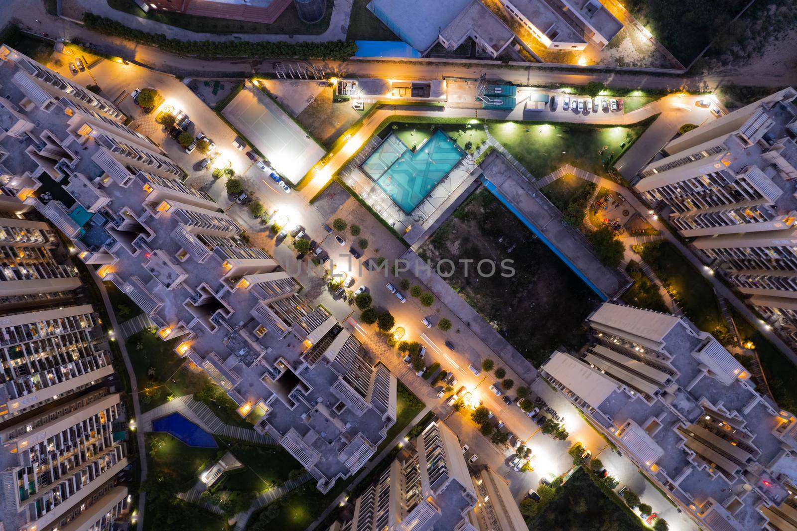 aerial drone shot ooking down over skyscrapers of a premium apartment complex with parking swimming pools with lights switched on at dusk twilight in gurgaon haryana India drone shot