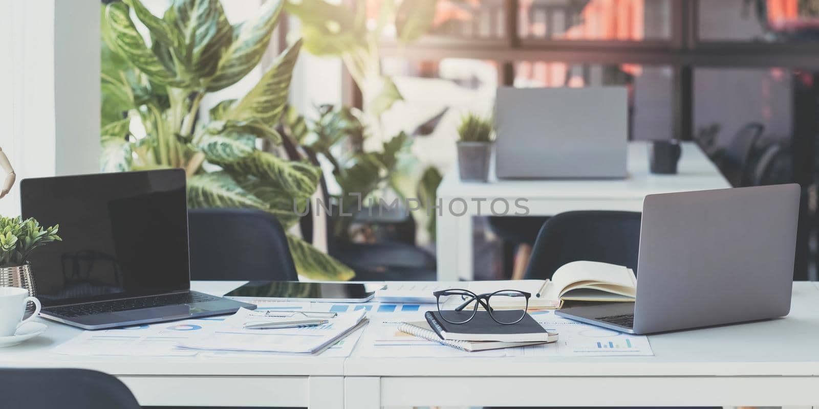 Laptop Computer, notebook, and eyeglasses sitting on a desk in a large open plan office space after working hours by wichayada