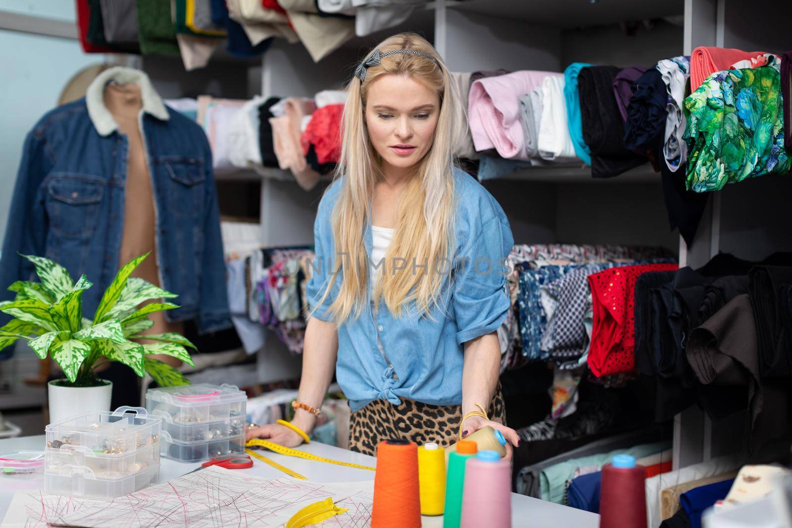 A blonde woman at a tailor shop is trying to choose the right thread color for her next blouse. A women's clothing designer.