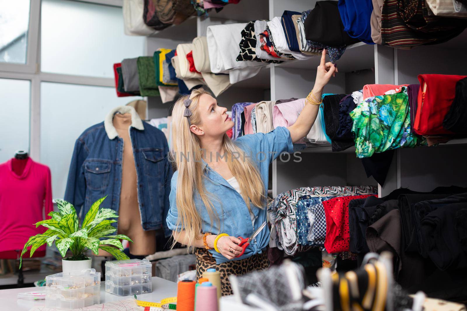 A woman checks the fabric rack to see if she will have the right color of fabric for her next collection. A blonde woman with fair skin.