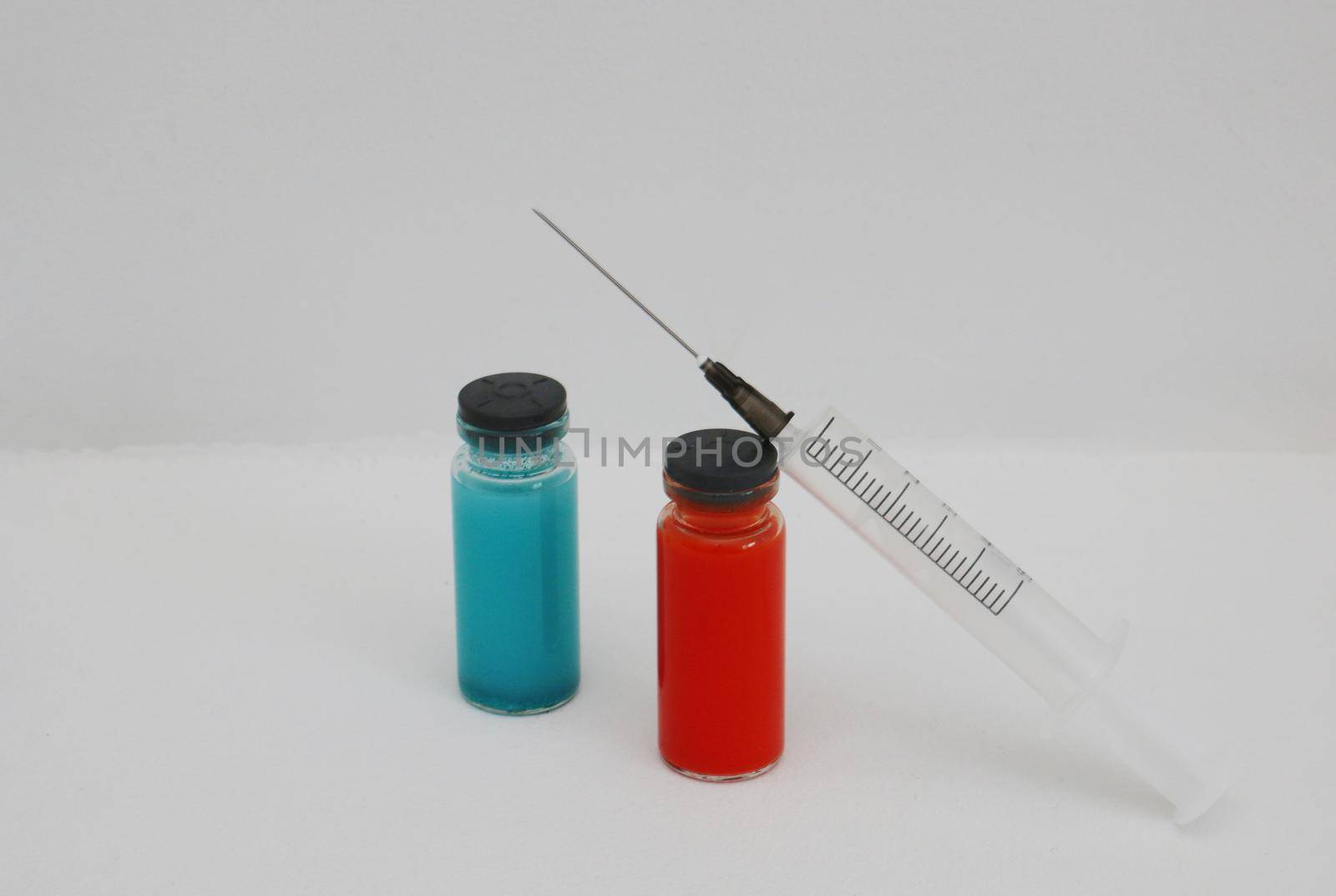 Red and blue medicine bottle and disposable injection syringe. Two ampoules with covid-19 vaccine and a syringe on a white background.