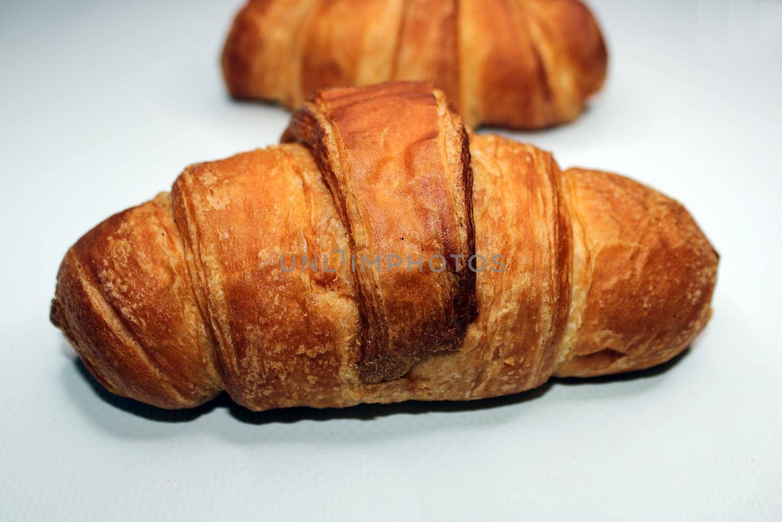 Fresh crispy croissant close-up on a light background. Blurred croissant in the background. Cooking, home baking.