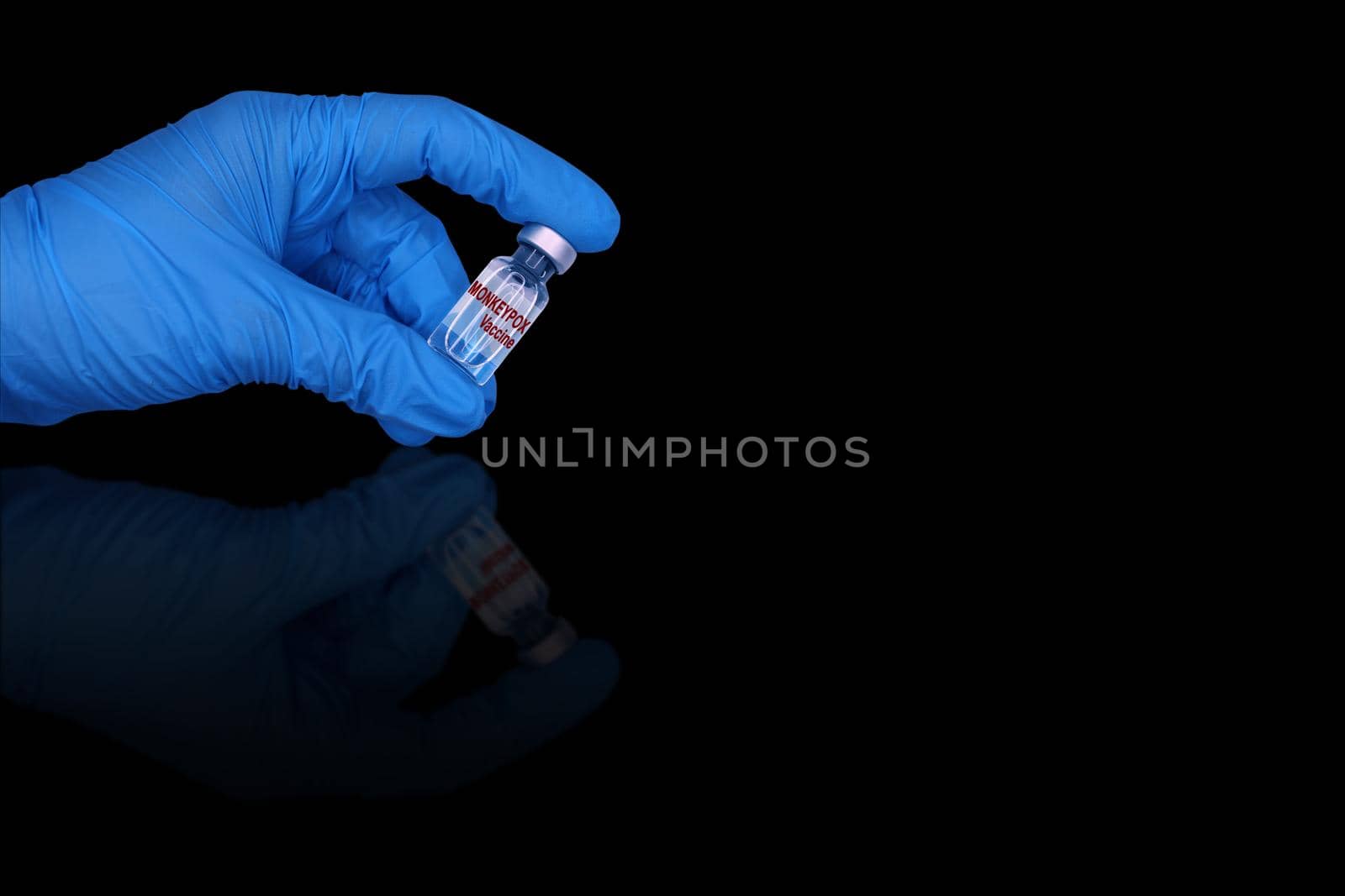 The monkeypox vaccine in a hand in a blue medical glove on a black mirror background.