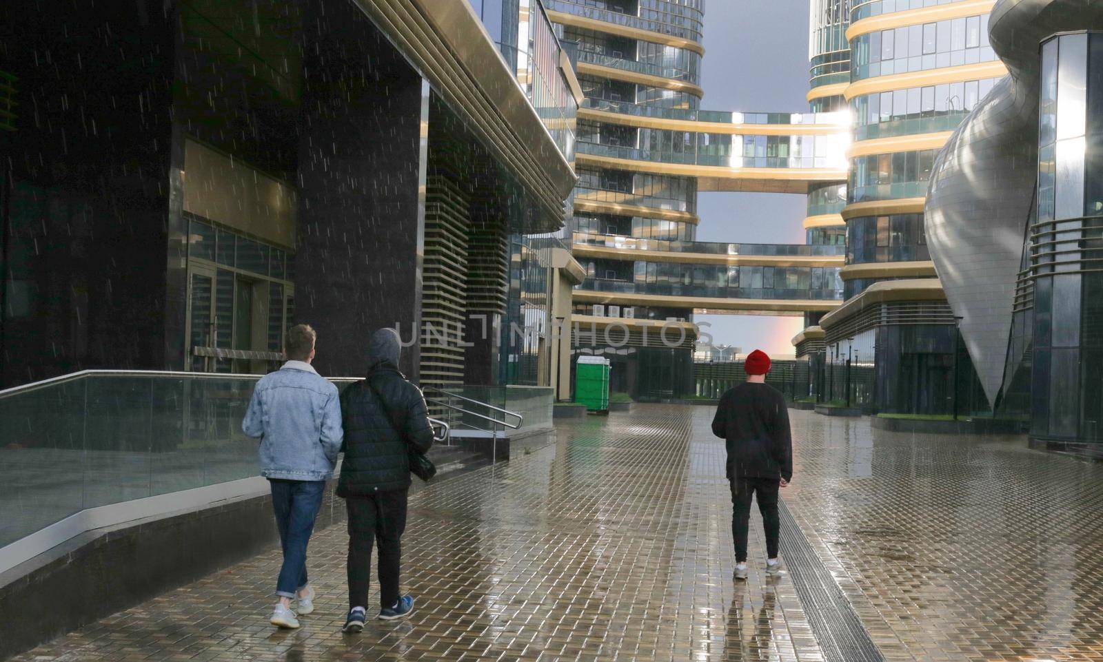 Walking people on the background of skyscrapers in the rain. Glare on glass.