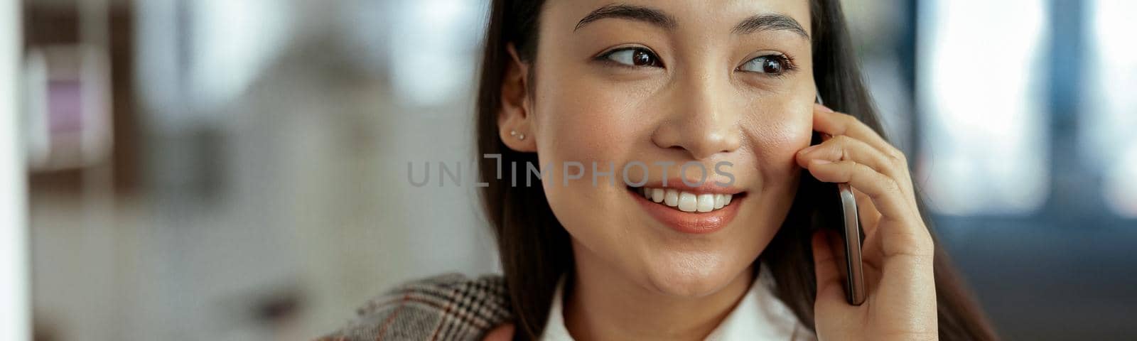 Close up of smiling asian business woman making phone call standing at office by Yaroslav_astakhov