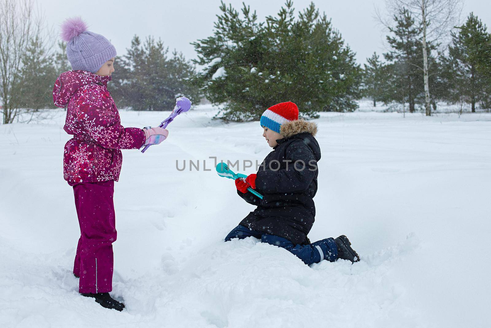 A boy and a girl are outdoors in winter, making snowballs with plastic sculpting tools. Copy space