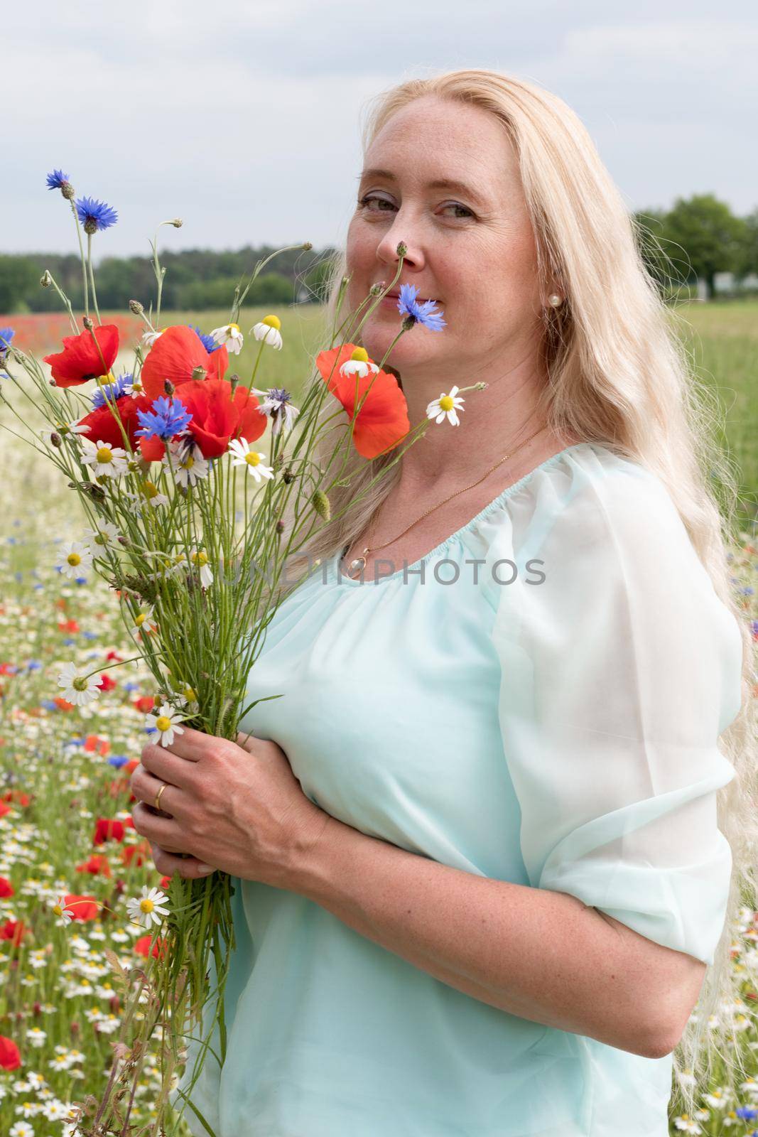 beautiful middle-aged blonde woman stands among a flowering field of poppies by KaterinaDalemans