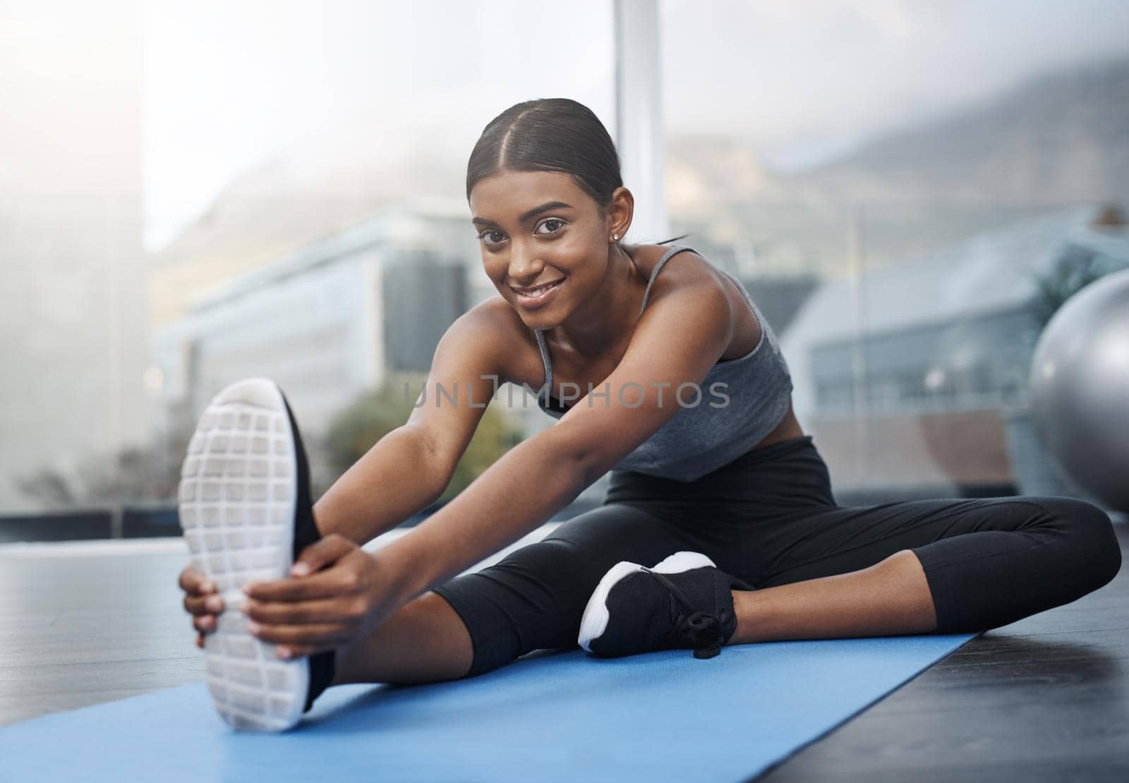 Sometimes all you need to do is smile through it. a beautiful young woman smiling while sitting down and doing stretching exercises on her gym mat at home. by YuriArcurs