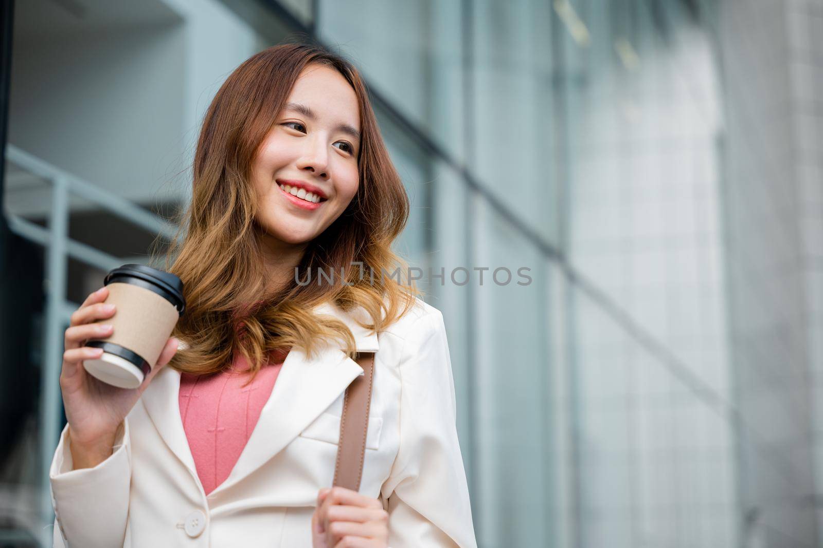 Asian businesswoman holding coffee cup takeaway going to work she walking near her office building, Portrait smiling business woman hold paper cup of hot drink outdoor walking on street