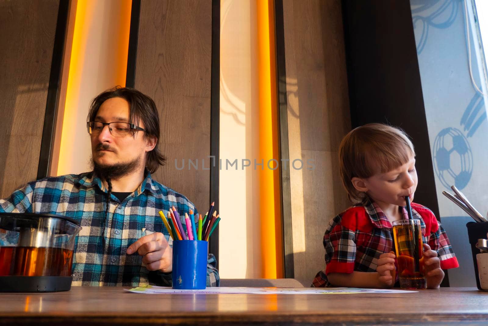 a child with his father in a restaurant draws a coloring book, waiting for cooking